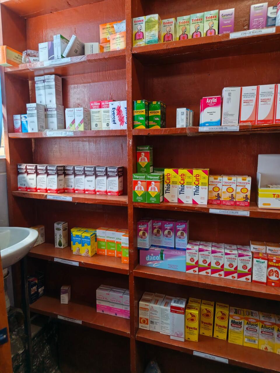 Labelled pharmacy shelves at Primegala: antibiotics, antibiotic syrups, cough syrups and antacids